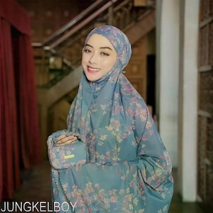 May include: A woman wearing a blue floral patterned prayer garment and matching head covering. The garment has a floral design in shades of pink and yellow. A small matching pouch is held in the hand. The text "JUNGKELBOY" is at the bottom of the image.