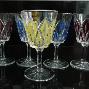 May include: Five stemmed wine glasses with cut glass designs. The glasses are decorated with coloured bands of red, yellow, and blue.