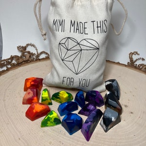 May include: A white drawstring bag with the text "Mimi Made This" and a geometric heart design. The bag is filled with colorful and black and white crayon-like shapes.