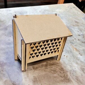 May include: A small wooden box with a heart-shaped cutout design on the front. The box is made of light brown wood and has a simple, rustic look.