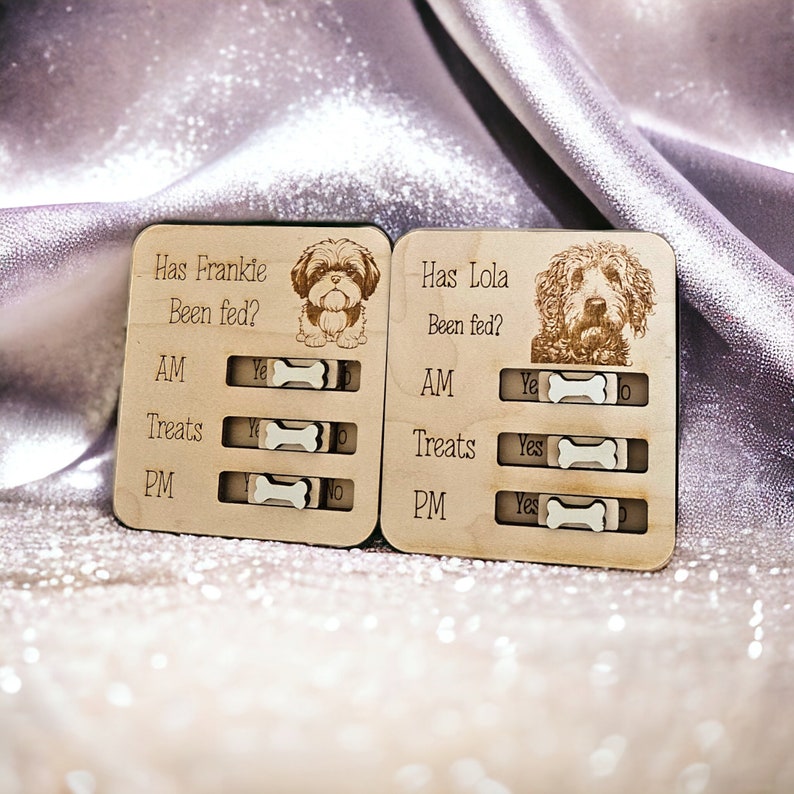 May include: Two wooden dog treat tracker boards with a dog's picture and the text "Has Frankie Been Fed?" and "Has Lola Been Fed?" with "AM", "Treats", and "PM" labels and "Yes" and "No" toggles.