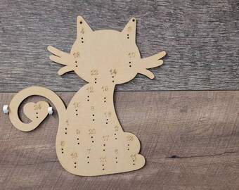 Puede incluir: Proyecto de artesanía de madera en forma de gato con agujeros numerados para enhebrar cuentas. El gato tiene una cola en forma de corazón con el número 24.
