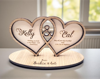 May include: Wooden anniversary decoration featuring two interlocking hearts. The names "Kelly" and "Cal" are engraved on the hearts, along with anniversary wishes. The base is round and also engraved.