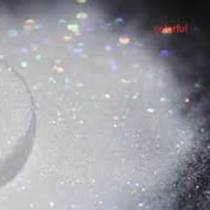 May include: A close-up of white glitter, with a small round container of the glitter in the foreground.