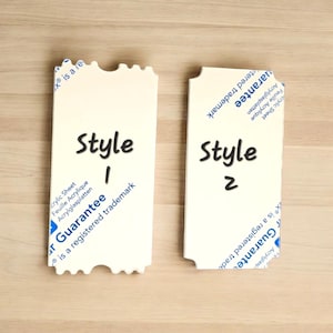 May include: Two white ticket-shaped signs with a jagged edge. The sign on the left says "Style 1" and the sign on the right says "Style 2". Both signs have text about acrylic sheets and a guarantee.