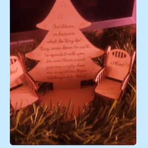 Puede incluir: Un adorno de &aacute;rbol de Navidad de madera con un mensaje sobre seres queridos en el cielo. El adorno presenta dos peque&ntilde;as sillas de madera con las palabras "Pap&aacute;" y "Mam&aacute;" en ellas. El &aacute;rbol est&aacute; rodeado de oropel marr&oacute;n.