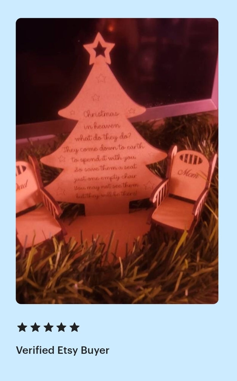 Puede incluir: Un adorno de &aacute;rbol de Navidad de madera con un mensaje sobre seres queridos en el cielo. El adorno presenta dos peque&ntilde;as sillas de madera con las palabras "Pap&aacute;" y "Mam&aacute;" en ellas. El &aacute;rbol est&aacute; rodeado de oropel marr&oacute;n.
