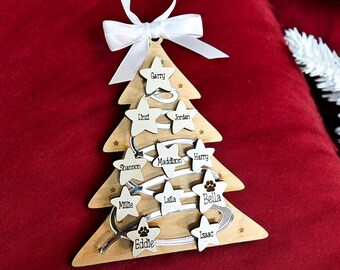 Puede incluir: Un adorno de árbol de Navidad de madera con una cinta blanca y los nombres Garry, Linzi, Jordan, Madison, Harry, Shannon, Millie, Lalla, Bella, Eddie e Isaac en él.