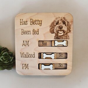 May include: Wooden pet care tracker with a photo of a dog and the text "Has Betty Been Fed" with a sliding bone to indicate "Yes" or "No" for AM, Walked, and PM.
