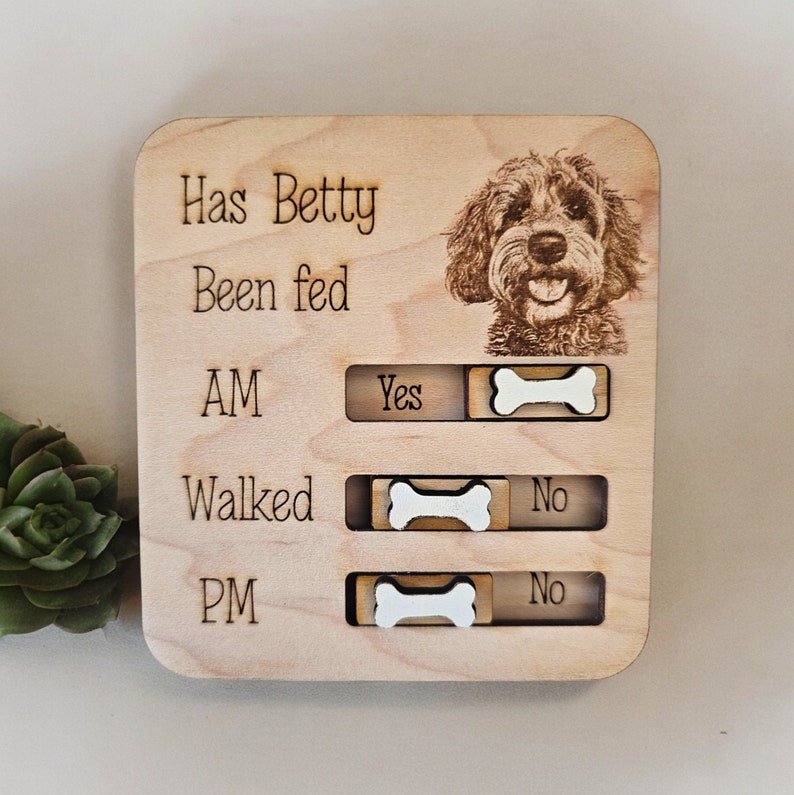 May include: Wooden pet care tracker with a photo of a dog and the text "Has Betty Been Fed" with a sliding bone to indicate "Yes" or "No" for AM, Walked, and PM.