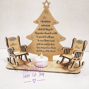 Puede incluir: Adorno de &aacute;rbol de Navidad de madera con dos mecedoras, una etiquetada como "Mam&aacute;" y la otra como "Pap&aacute;". El &aacute;rbol tiene una cita sobre la Navidad en el cielo y un portavelas de t&eacute; en la base. El adorno est&aacute; hecho por The Snappy Laser Cut Shop.