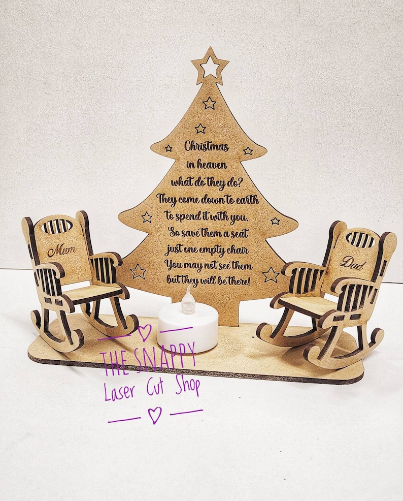 Puede incluir: Adorno de &aacute;rbol de Navidad de madera con dos mecedoras, una etiquetada como "Mam&aacute;" y la otra como "Pap&aacute;". El &aacute;rbol tiene una cita sobre la Navidad en el cielo y un portavelas de t&eacute; en la base. El adorno est&aacute; hecho por The Snappy Laser Cut Shop.