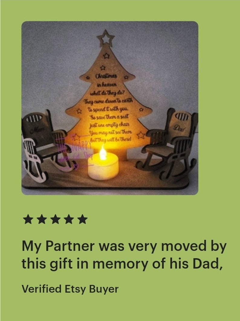 Puede incluir: Un adorno de &aacute;rbol de Navidad de madera con dos mecedoras, una etiquetada como "Mam&aacute;" y la otra como "Pap&aacute;". El &aacute;rbol tiene una cita sobre los seres queridos en el cielo y una vela encendida frente a &eacute;l.