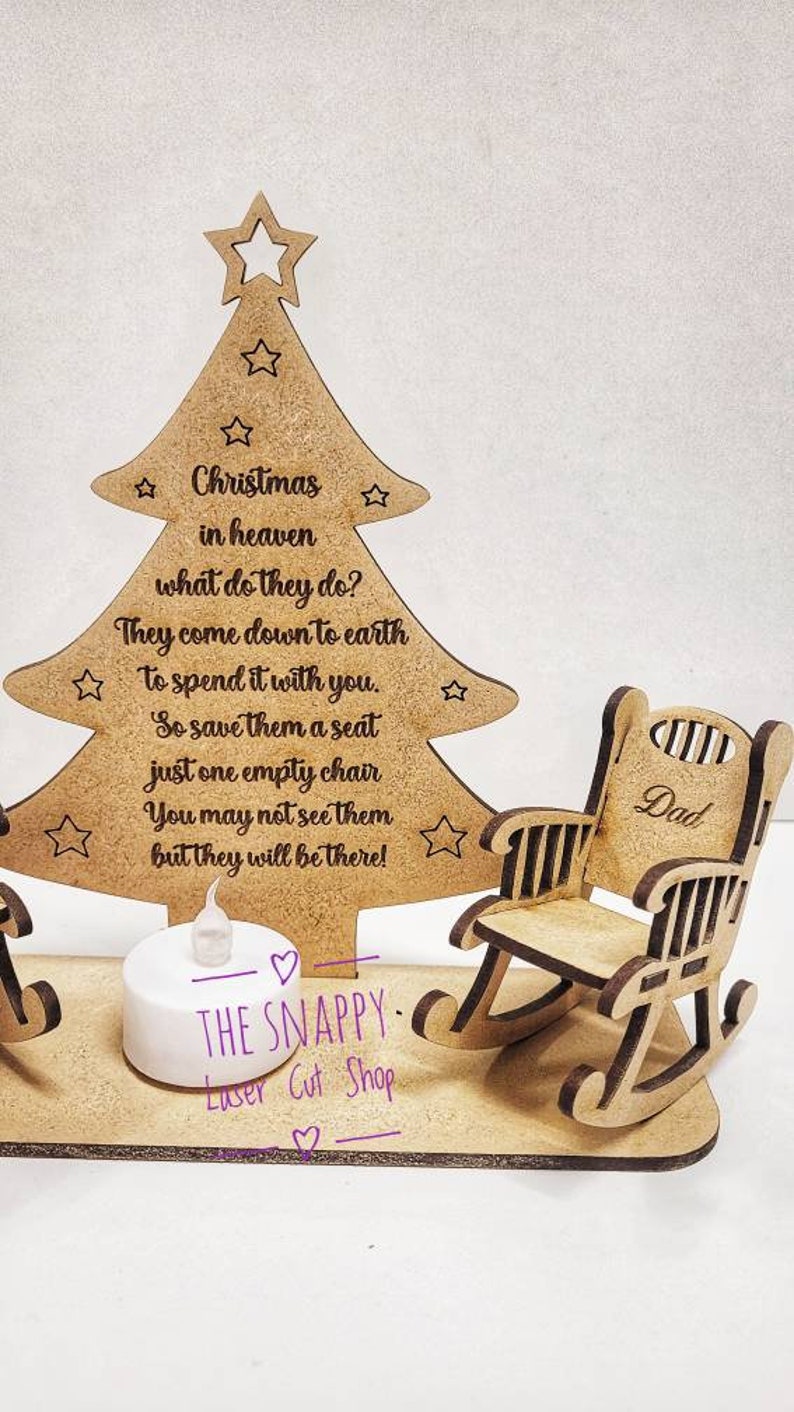 Puede incluir: Adorno de &aacute;rbol de Navidad de madera con dos mecedoras, una etiquetada como "Pap&aacute;". El &aacute;rbol tiene una cita sobre los seres queridos en el cielo que bajan a la tierra para pasar la Navidad contigo. El adorno incluye una peque&ntilde;a luz de t&eacute; LED.