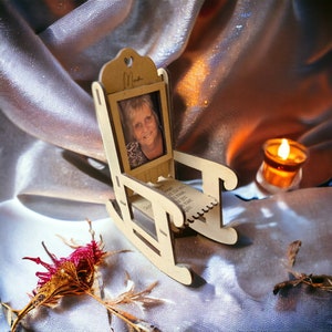 May include: A wooden rocking chair with a photo frame inset. The frame contains a photo of a woman with blonde hair. The chair is sitting on a white fabric surface. The text "Mum" is written on the chair.