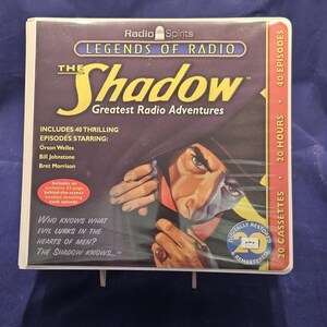 May include: A boxed set of "The Shadow: Greatest Radio Adventures" on cassette tapes. The cover features a dramatic illustration of a man in a fedora. The set includes 40 episodes, starring Orson Welles, Bill Johnstone, and Bret Morrison.