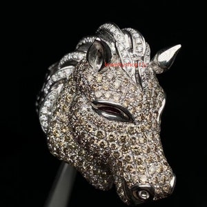 Puede incluir: Un anillo de plata con forma de unicornio con un diseño detallado, cubierto de pequeños diamantes brillantes. La cabeza del unicornio está mirando hacia adelante, con su cuerno apuntando hacia arriba.