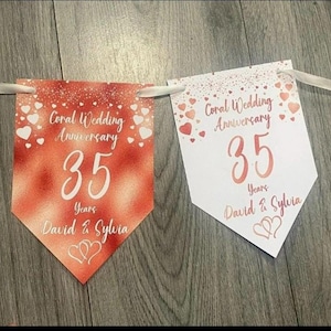 Op de afbeelding: Twee wimpelbanners voor een koraal trouwdag. Eén banner is rood, de andere wit. Beide banners tonen de tekst "Koraal Huwelijksverjaardag 35 Jaar David & Sylvia" in koraal, met hartjes.