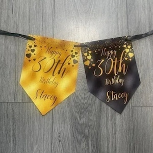 Op de afbeelding: Een zwart en gouden banner met de tekst "Happy 30th Birthday Stacey" op elke vlag. De vlaggen zijn versierd met gouden harten.