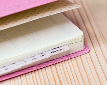 May include: A pink weekly planner with the text "BONICHI AHO 2022" and "Weeks" printed on the cover. The planner has pink tabs for each month of the year.