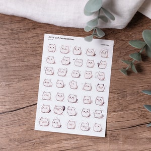 Puede incluir: Una hoja de pegatinas con 36 expresiones de gato diferentes. Las pegatinas son blancas con contornos negros y varias expresiones faciales. La hoja está etiquetada como "Cute Cat Expressions" y "COSMICA".