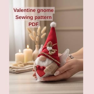 Peut inclure: Un patron de couture de gnome de la Saint-Valentin au format PDF. Le gnome a un chapeau rouge avec un pompon blanc, une barbe blanche et un cœur rouge. Il a des ailes blanches et est tenu dans les mains de quelqu'un. Le texte "Valentine gnome Sewing pattern PDF" est dans l'image.
