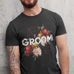 May include: A black t-shirt with a floral design and the word "GROOM" printed in white. The flowers are red, yellow, and white.