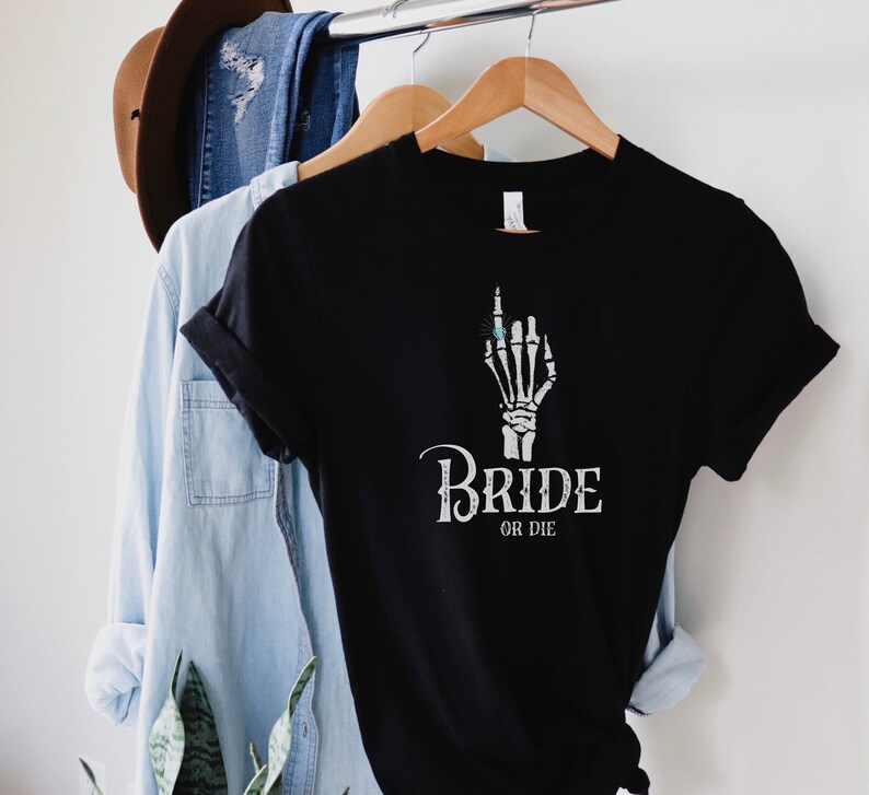 May include: Black t-shirt featuring a white skeleton hand wearing a ring and the text "Bride or Die".