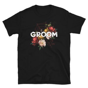 May include: Black t-shirt with a floral design and the word "GROOM" in white letters.