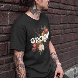 May include: Black t-shirt with a floral design and the word "GROOM" printed in white. The flowers are red, pink, yellow, and white.