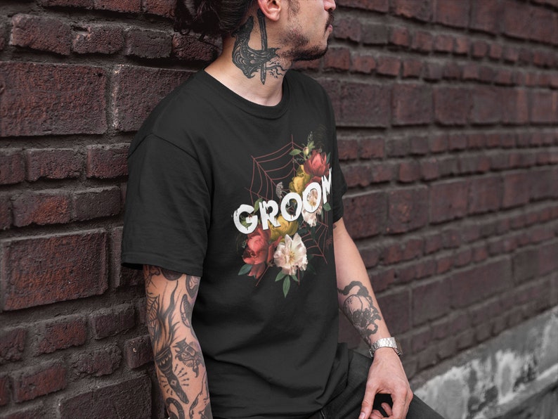 May include: Black t-shirt with a floral design and the word "GROOM" printed in white. The flowers are red, pink, yellow, and white.