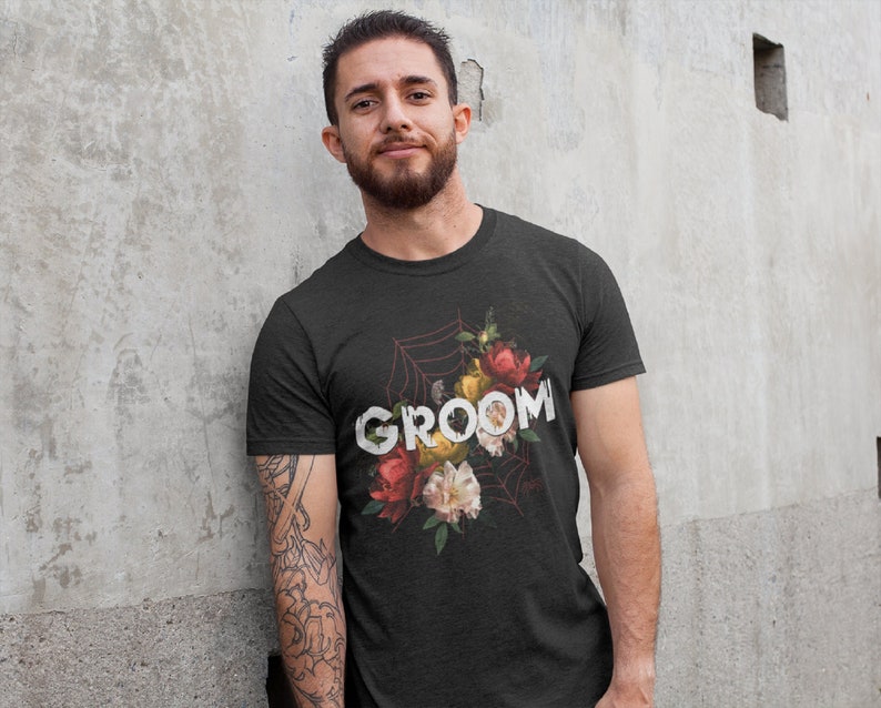 May include: A black t-shirt with a floral design and the word "GROOM" printed in white. The flowers are red, yellow, and white.