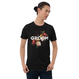 May include: Black t-shirt with a floral design and the word "GROOM" printed in white. The flowers are red, yellow, and white.