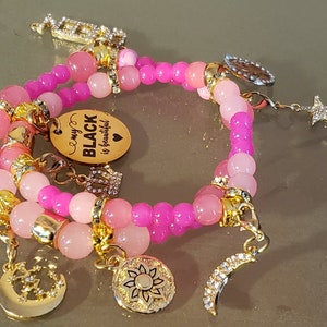 May include: A pink and gold bracelet with charms, including a charm that says "My Black is Beautiful".