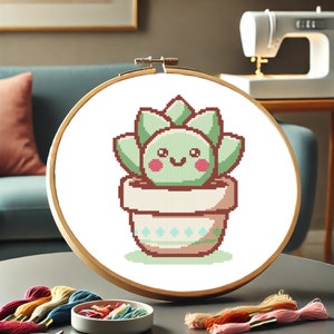 Peut inclure: Un cercle de broderie au point de croix avec un cactus souriant en pot. Le cactus est vert clair avec des joues roses, et le pot est beige avec un motif de losanges turquoise. Le cercle en bois est présenté avec du fil à broder coloré.