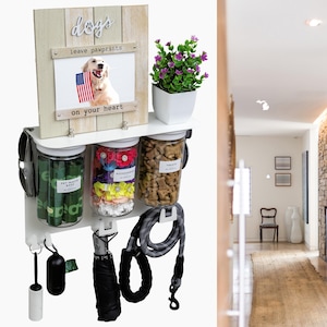 Peut inclure: Organiseur mural blanc pour les fournitures pour chiens avec trois bocaux transparents, une laisse, un distributeur de sacs à crottes et un porte-sacs à crottes pour chiens. Les bocaux sont étiquetés "Friandises", "Accessoires" et "Sacs à déjections canines". Une photo encadrée avec le texte "Les chiens laissent des empreintes de pattes sur votre cœur" est au-dessus des bocaux. Une plante en pot est à gauche de la photo.