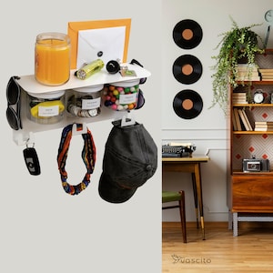 Könnte beinhalten: Weißer Wandorganizer mit drei durchsichtigen Gläsern, die mit "Schlüssel", "Kleingeld" und "Leckerlis" beschriftet sind. Die Gläser sind mit verschiedenen Gegenständen gefüllt, darunter Schlüssel, Münzen und Süßigkeiten. Es gibt auch Haken zum Aufhängen von Gegenständen wie einem Hut, einem Schal und einer Sonnenbrille. Der Organizer ist an einer weißen Wand montiert.