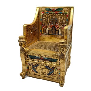 以下が含まれることがあります： エジプトをテーマにした複雑な彫刻が施された、金色の装飾的な椅子。 椅子には象形文字、人物、詳細な背もたれがあります。 アームレストは彫刻された人間の頭で飾られ、脚はライオンの足で終わっています。