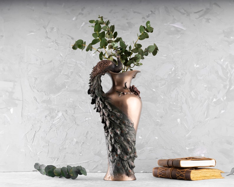 Puede incluir: Un jarr&oacute;n decorativo con forma de pavo real con acabado en cobre. El jarr&oacute;n est&aacute; lleno de hojas de eucalipto verdes.