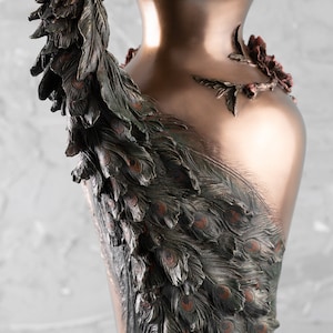 Puede incluir: Un jarr&oacute;n de color bronce con un dise&ntilde;o de pavo real. El jarr&oacute;n est&aacute; decorado con detalles intrincados, incluyendo plumas y un motivo floral.