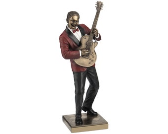 May include: A bronze sculpture of a man playing a guitar. He is wearing a red jacket and black pants. The sculpture is on a square base.
