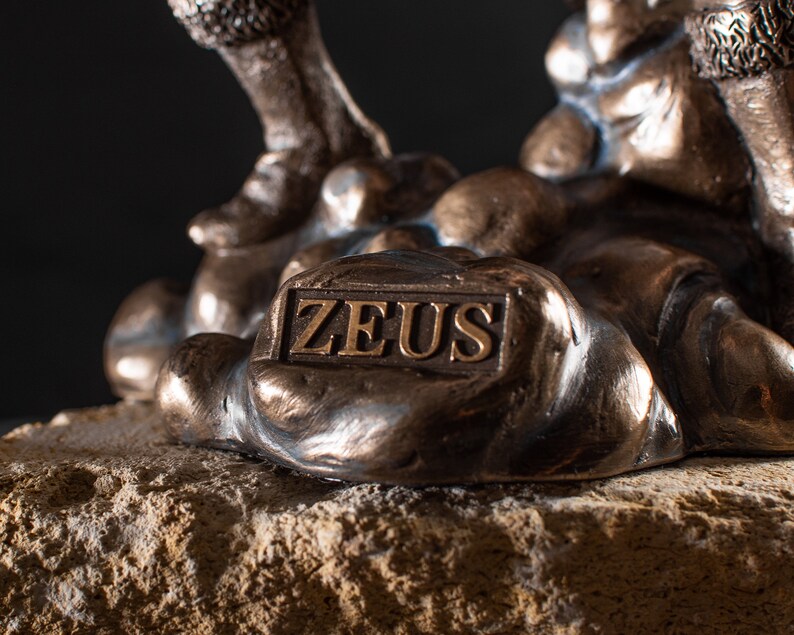 K&ouml;nnte beinhalten: Bronzeskulptur von Zeus, dem griechischen Gott des Himmels und des Donners, stehend auf einem felsigen Sockel. Die Skulptur ist detailliert und tr&auml;gt eine Inschrift auf dem Sockel, die "ZEUS" lautet.