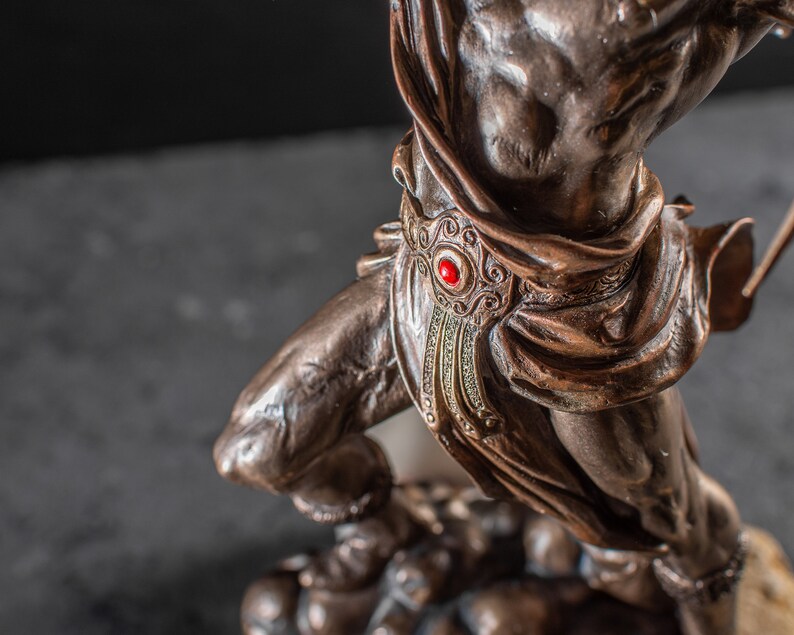 K&ouml;nnte beinhalten: Bronzeskulptur einer Kriegerfigur mit einem roten Juwel am G&uuml;rtel. Der Krieger steht auf einem Sockel mit anderen Figuren.