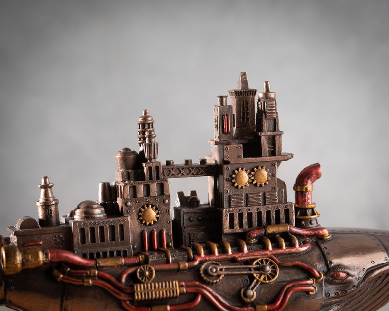 Op de afbeelding: Een steampunk-walfiguur met ingewikkelde details, waaronder tandwielen, pijpen en een rode schoorsteen. De walvis is gemaakt van metaal en heeft een bronzen afwerking.