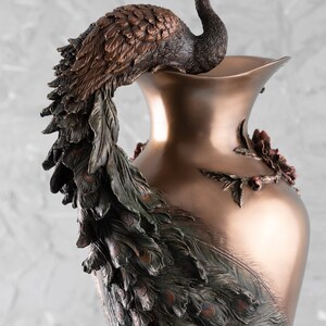 Puede incluir: Un jarr&oacute;n decorativo con un dise&ntilde;o de pavo real. El jarr&oacute;n est&aacute; hecho de metal y tiene un acabado bronce. Las plumas de la cola del pavo real est&aacute;n extendidas y cubren todo el jarr&oacute;n.