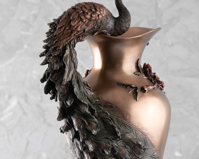 Puede incluir: Un jarr&oacute;n decorativo con un dise&ntilde;o de pavo real. El jarr&oacute;n est&aacute; hecho de metal y tiene un acabado bronce. Las plumas de la cola del pavo real est&aacute;n extendidas y cubren todo el jarr&oacute;n.