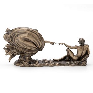 May include: A bronze-toned sculpture depicting two figures reaching toward each other with extended fingers. One figure is partially obscured by swirling, draped fabric, while the other figure is seated on a textured base. The piece has a metallic finish.