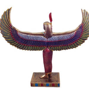 May include: A gold-colored statue of the Egyptian goddess Isis with outstretched wings. The wings are decorated with green, blue, and gold details. The statue is standing on a base with blue, red, and gold stripes.