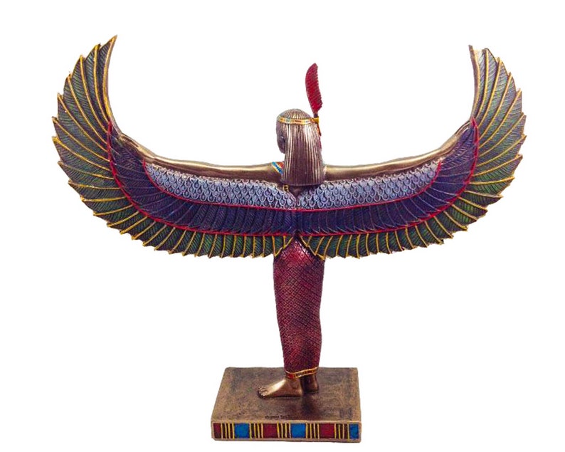 May include: A gold-colored statue of the Egyptian goddess Isis with outstretched wings. The wings are decorated with green, blue, and gold details. The statue is standing on a base with blue, red, and gold stripes.