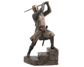 May include: Bronze-colored statue of a medieval knight in full armor, raising a sword overhead. The knight stands on a stone base, with a red cross emblem on the chest. The statue is detailed and realistic, capturing the knight's pose.